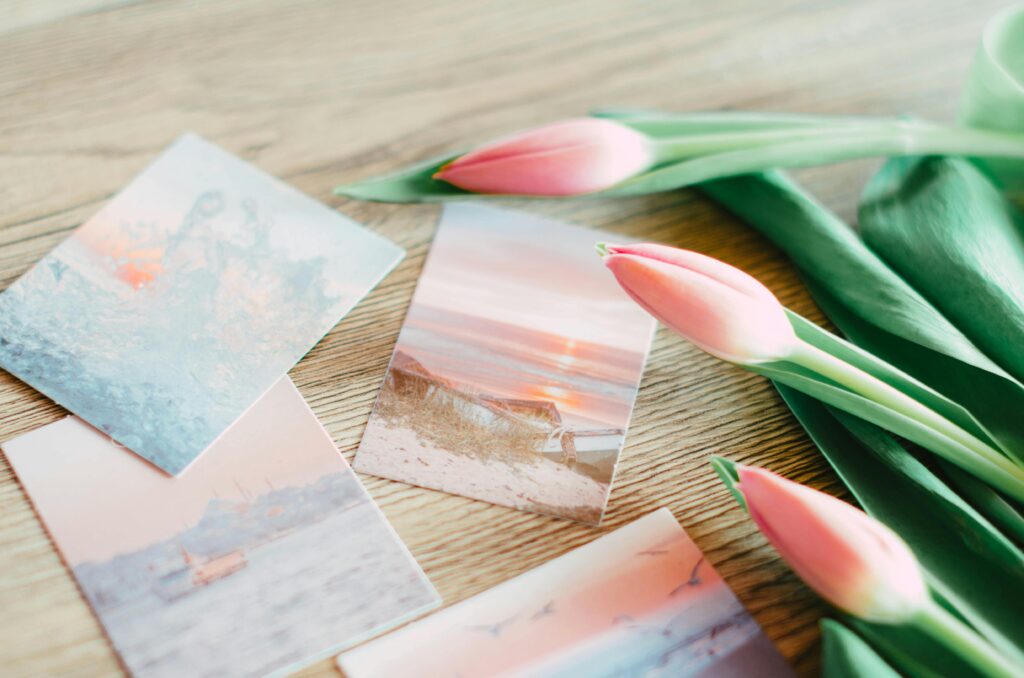 Pink tulips and artistic postcards on a wooden table create a serene still life scene.